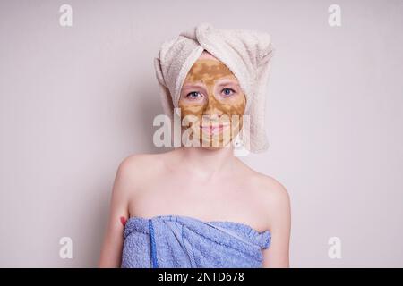 jeune femme avec la terre curative ou l'argile beauté masque facial, un traitement ayurveda naturel pour l'acné ou la peau grasse, enveloppé dans une serviette Banque D'Images