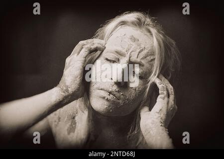 visage de la femme couverte d'un masque sec en argile craquelée tenant sa tête dans la douleur, image granuleuse filtrée créative Banque D'Images