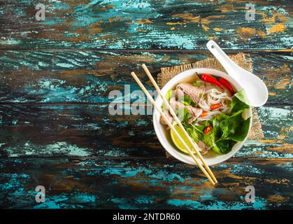 Soupe traditionnelle vietnamienne Pho bo avec des herbes, de la viande, des nouilles de riz, de bouillon. Pho bo dans un bol avec des baguettes, cuillère. L'espace pour le texte. Vue d'en haut. Soupe Asiatique Banque D'Images