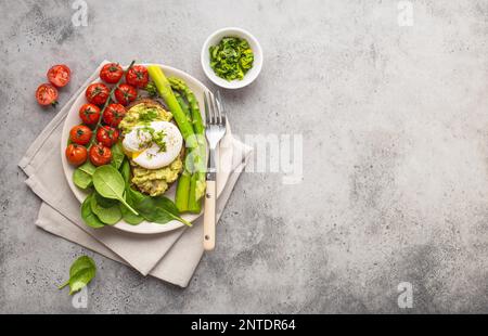 Repas végétarien sain. Toast, avocat, œuf poché, asperges, tomates cuites au four, épinards. Arrière-plan en pierre. Espace pour le texte. Végétarien Banque D'Images