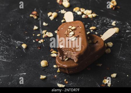 Pop-sutes au chocolat au lait et aux noisettes. Gros plan. Crèmes glacées, crèmes glacées, papillotes recouvertes de chocolat, bâtonnets, fond de pierre noire. Mise au point sélective. Banque D'Images