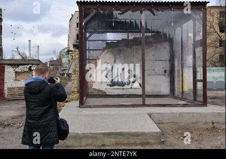 Borodyanka, Ukraine. 26th févr. 2023. Un homme prend des photos du travail de Banksy avec son téléphone, le travail de l'artiste anglais Banksy est visible sur le mur détruit, après que la Fédération de Russie a attaqué la ville de Borodyanka, les autorités ont décidé de sauver le travail de Banksy et maintenant ils sont protégés par le système. Crédit : SOPA Images Limited/Alamy Live News Banque D'Images