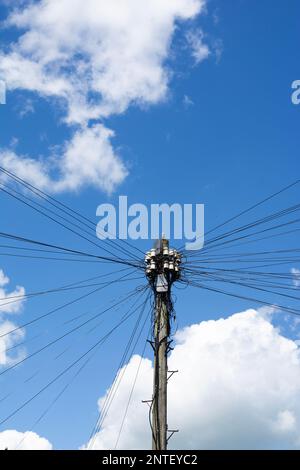 un vieux poteau électrique en bois avec une propagation de lignes électriques contre un ciel bleu Banque D'Images