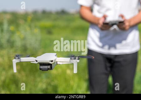 Un homme un pilote de drone avec un panneau de commande dans ses mains contrôle un quadricoptère dans le champ d'été en extérieur Banque D'Images