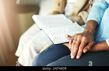 Mains, bible et couple senior priant dans leur maison ensemble pour l'écriture, la foi et la confiance. Famille, culte et louange avec homme et femme âgés Banque D'Images