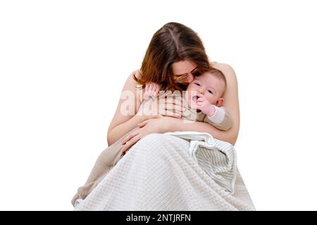 Une mère femme embrasse et réconforte un bébé garçon pleurant assis sur le lit, isolé sur un fond blanc. Enfant de 6 mois Banque D'Images