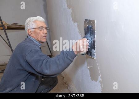 un vieil homme tenant une truelle de bois est plâtrage mur de ciment à la maison, concept un hobby dans les personnes âgées.pensioner travailleur plâtrage le wall.senior travailleur Banque D'Images