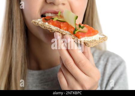 Femme mangeant du pain de seigle frais avec fromage à la crème, saumon et concombre sur fond blanc, gros plan Banque D'Images