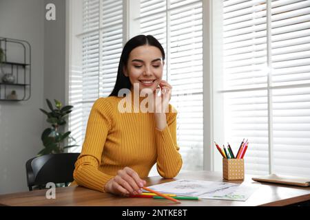 Jeune femme colorant la page antistress à la table à l'intérieur Banque D'Images