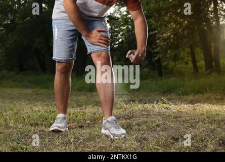 Homme appliquant un insectifuge sur la jambe dans le parc, gros plan. Prévention des piqûres de tiques Banque D'Images