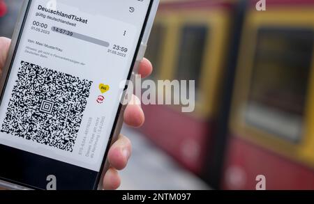 Berlin, Allemagne. 27th févr. 2023. Sur l'écran d'un smartphone, le code QR du Nationwide Deutschland-Ticket est affiché à côté des logos de VBB et BVG, tandis qu'un train S-Bahn passe en arrière-plan. Credit: Monika Skolimowska/dpa/Alay Live News Banque D'Images