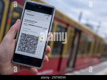 Berlin, Allemagne. 27th févr. 2023. Sur l'écran d'un smartphone, le code QR du Nationwide Deutschland-Ticket est affiché à côté des logos de VBB et BVG, tandis qu'un train S-Bahn passe en arrière-plan. Credit: Monika Skolimowska/dpa/Alay Live News Banque D'Images