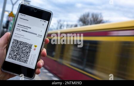 Berlin, Allemagne. 27th févr. 2023. Sur l'écran d'un smartphone, le code QR du Nationwide Deutschland-Ticket est affiché à côté des logos de VBB et BVG, tandis qu'un train S-Bahn passe en arrière-plan. Credit: Monika Skolimowska/dpa/Alay Live News Banque D'Images