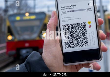 Berlin, Allemagne. 27th févr. 2023. Sur l'écran d'un smartphone, le code QR du Nationwide Deutschland-Ticket est affiché à côté des logos de VBB et BVG, tandis qu'un train S-Bahn passe en arrière-plan. Credit: Monika Skolimowska/dpa/Alay Live News Banque D'Images