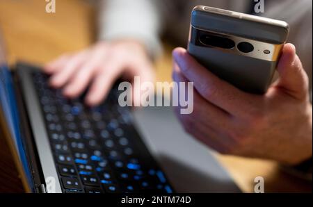 Berlin, Allemagne. 27th févr. 2023. Un homme s'assoit à l'ordinateur portable et tient un smartphone dans la main. Credit: Monika Skolimowska/dpa/Alay Live News Banque D'Images