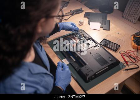 Réparateur fille de démonter la carte mère de l'ordinateur portable et d'installer la puce de mémoire. Un technicien répare un ordinateur cassé au travail dans un ancien atelier de réparation. Réparation électronique Banque D'Images