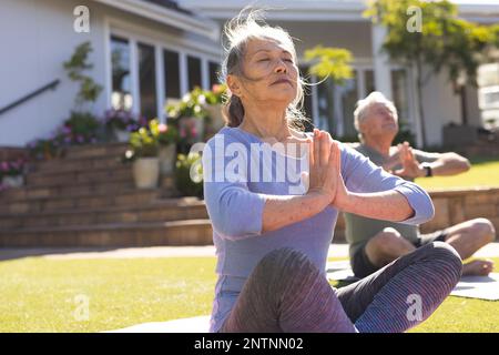 Heureux senior divers couple faisant du yoga et méditant dans le jardin Banque D'Images