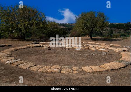 Des anneaux de dalles de pierre marquent les fondations d'un tholos, une ancienne structure en dôme entourée de colonnes, dans la Valle dei Templi ou la Vallée des temples à Agrigento, dans le sud de la Sicile, en Italie. Sept temples doriques monumentaux datant d'environ 580 av. J.-C. survivent ici au milieu des ruines de la ville Graeco-romaine d'Akragas ou d'Agrigentum. Banque D'Images