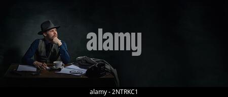 Détective professionnel en chapeau fedora assis à table avec une expression sérieuse et réfléchie sur fond vert foncé vintage. Bannière Banque D'Images
