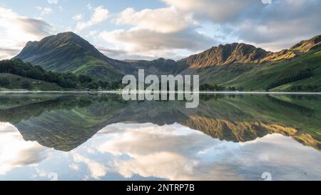 Lac de Buttermere dans le Lake District avec la ligne d'arbre au bord de l'eau et une couche de brume produisant un beau reflet des montagnes. Banque D'Images