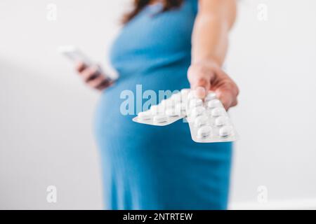 femme enceinte tenant des comprimés de multivitamines dans sa main et montrant sa bosse au dernier stade de la grossesse Banque D'Images