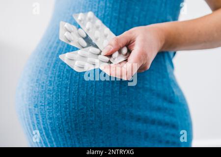 femme enceinte tenant des comprimés de multivitamines dans sa main et montrant sa bosse au dernier stade de la grossesse Banque D'Images