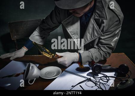 Image rognée d'un détective masculin regardant dans la loupe les empreintes sur la tasse à café, trouvant des indices de cas. Enquête professionnelle Banque D'Images