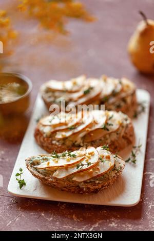 roquefort de fromage français et de tranches de pêches toasts sur une assiette carrée, sur une table sous des fleurs mimosa Banque D'Images