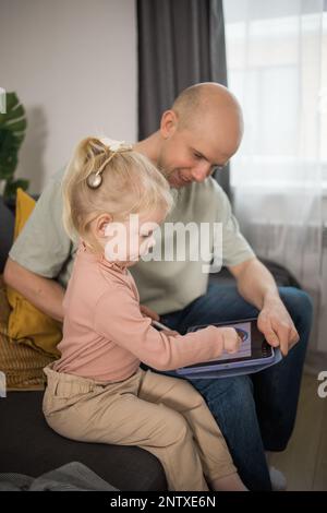 Personnes équipées d'un système d'implant cochléaire. Enfant étudie pour entendre avec son père, apprenant avec la vidéo sur tablette. Installation de l'implant cochléaire sur l'oreille de l'enfant Banque D'Images