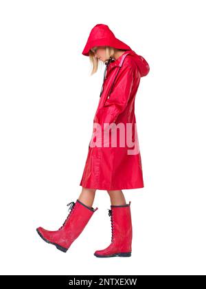 Pourquoi pleut-il toujours sur moi. Femme portant un imperméable rouge, un chapeau et des bottes avec sa tête vers le bas et les mains dans ses poches - pleine longueur. Banque D'Images