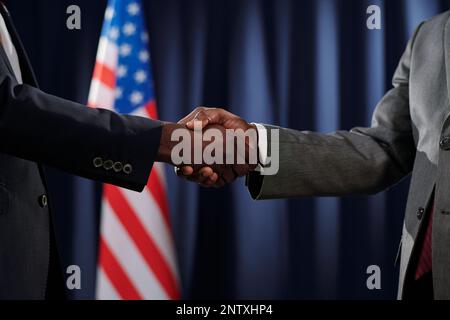 Deux délégués africains américains ou dirigeants politiques se serrant la main contre le drapeau des États-Unis tout en se tenant devant la caméra Banque D'Images