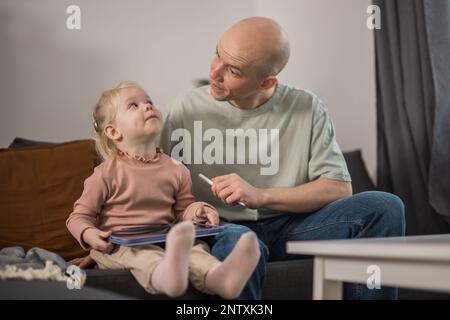 Personnes équipées d'un système d'implant cochléaire. Enfant étudier pour entendre avec son père drôle, apprendre avec la vidéo sur tablette. Installation d'un implant cochléaire sur un enfant Banque D'Images