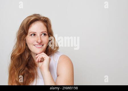 Portrait de femme REDHEAD. Magnifique modèle féminin avec des taches de rousseur qui regardent loin et sourient sur un fond blanc Banque D'Images