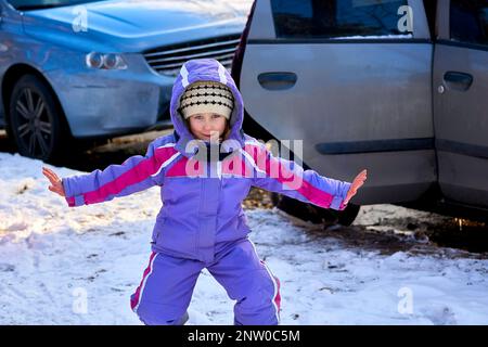 Un enfant mignon et gai en combinaison lilas se réjouit avant une promenade dans un parc d'hiver Banque D'Images