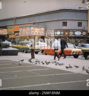 États-Unis New York 1964. Une scène de rue avec des voitures et des taxis en voiture sur Broadway dans le quartier de Times Square sur Manhattan. Les salles de cinéma affichent des heures de vol et un cri de bataille, tous deux créés aux États-Unis en octobre-novembre 1963. Un homme âgé est vu nourrir les pigeons. Crédit Roland Palm réf. 5-39-8 Banque D'Images