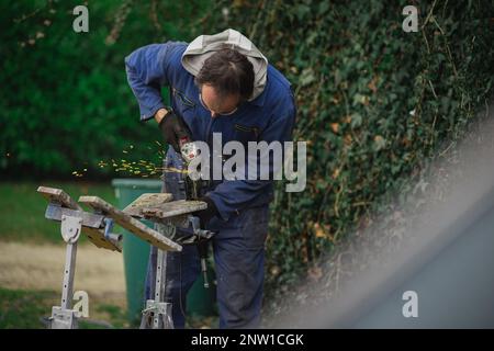 L'homme en combinaison bleue utilise une meuleuse d'angle pour découper des parties de métal. Des étincelles se sont envolantes. Banque D'Images