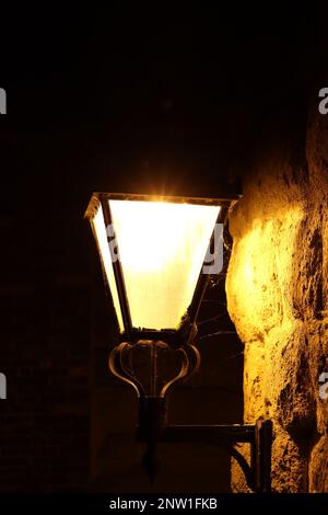 Lampadaire vintage brillamment éclairé la nuit contre un vieux mur de pierre Banque D'Images