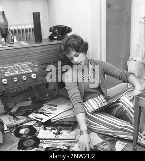 Les auditeurs de radio dans le passé. Une femme est vue sur le sol avec des disques par des chanteurs populaires et des groupes de 1950s.la radio combinée et le lecteur de disque est vu qui était un article populaire à ce moment-là, souvent un joli morceau de mobilier en lui-même, habituellement dans un coffret en bois. Elle est la chanteuse suédoise Lill-Babs Svensson. Suède 1958 réf. BV21-5 Banque D'Images