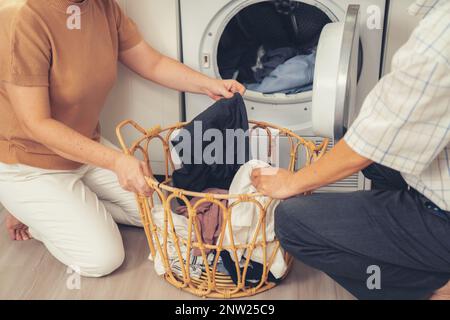 Couple senior travaillant ensemble pour compléter leurs tâches ménagères à la machine à laver de manière heureuse et agréable. Mari et femme faisant le Banque D'Images