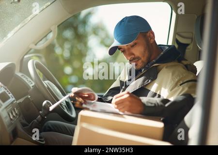 Mise à jour de son état de livraison. Photo d'un liveur qui lit des adresses tout en étant assis dans un fourgon de livraison. Banque D'Images