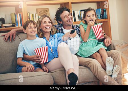 La soirée cinéma est leur tradition familiale préférée. Photo d'une famille heureuse regardant des films sur le canapé à la maison. Banque D'Images