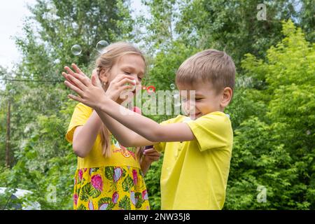 Les enfants heureux garçon et fille ont le plaisir dans le parc soufflant des bulles arc-en-ciel et des attraper et des éclater, l'été, jouer en plein air, avoir plaisir, conc de vacances Banque D'Images