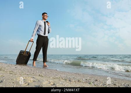 Bon homme d'affaires avec une valise à marcher sur la plage. Voyage d'affaires Banque D'Images