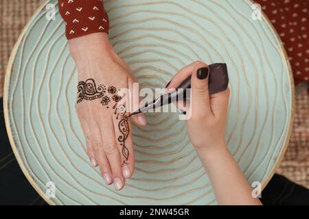 Maître mehndi professionnel faisant le tatouage au henné à la table, vue de dessus Banque D'Images