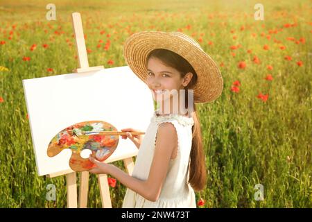 Petite fille peinture sur chevalet dans beau champ de pavot Banque D'Images