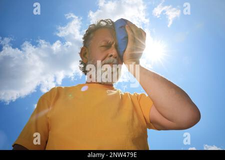 Homme âgé avec pack froid souffrant de coup de chaleur à l'extérieur, vue en angle bas Banque D'Images