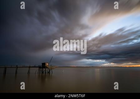 Cabane de pêche côtière sur pilotis en mer calme et nuages d'orage à l'horizon au coucher du soleil côte Atlantique France sur estuaire de la Gironde, Charente Maritime Banque D'Images