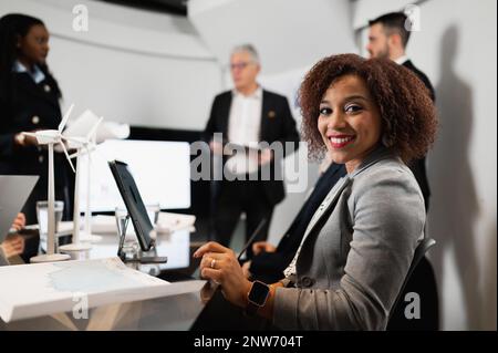 Femme d'affaires latine en gros plan qui regarde l'appareil photo sourire. Femme assise au bureau avec un ordinateur portable. Équipe travaillant pendant une réunion. Banque D'Images
