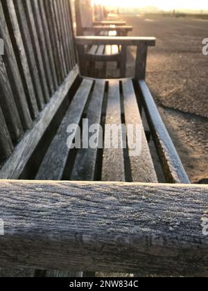 La lumière du matin se reflète sur l'accoudoir gelé glacé d'un banc de bord de mer d'autres bancs se dissolvent dans la distance automne, hiver, solitude romance Banque D'Images