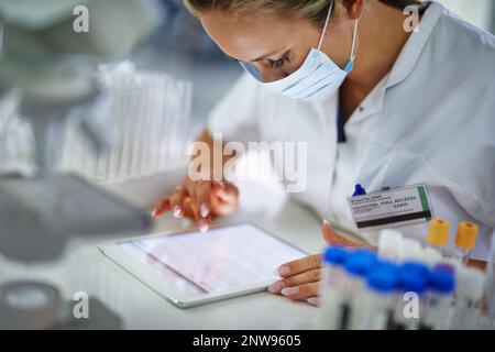 En vérifiant ses conclusions. Un jeune chercheur enregistre ses résultats sur une tablette dans le laboratoire. Banque D'Images